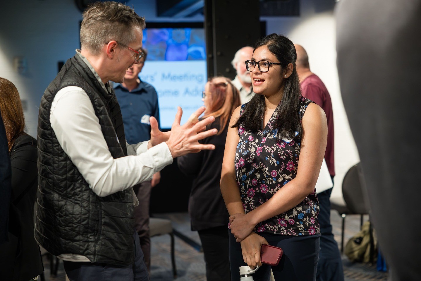 Two meeting attendees chat among others